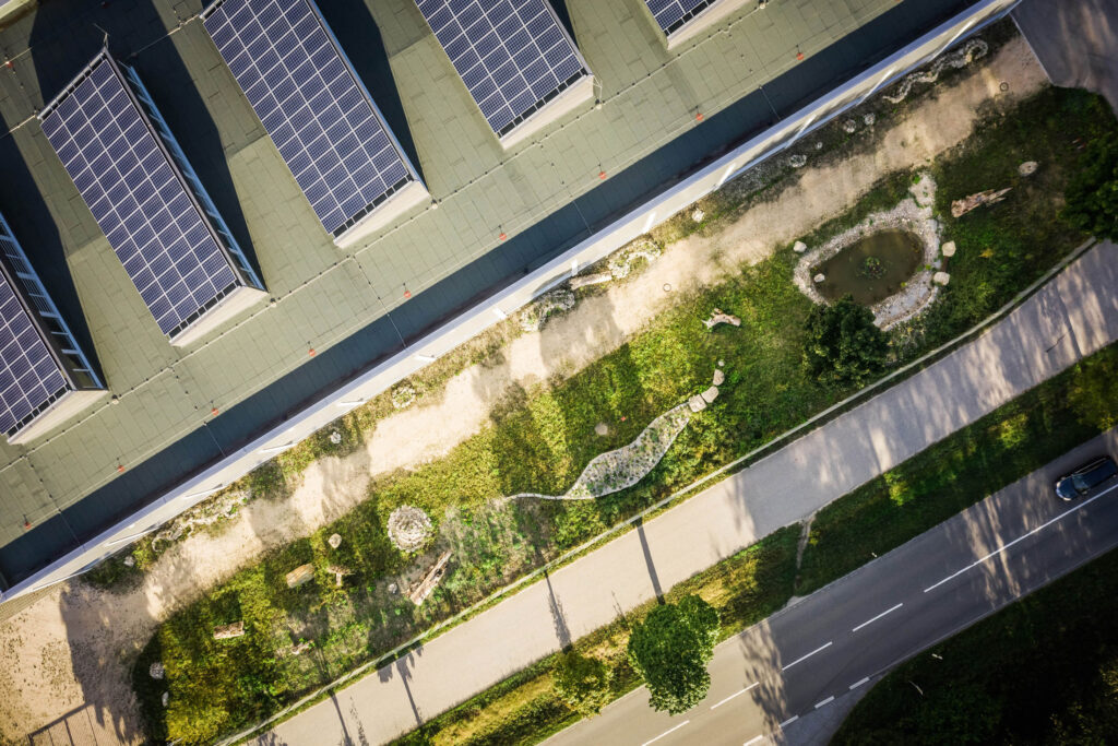 Dach mit Solarpanelen und naturnahes Betriebsgelände von oben