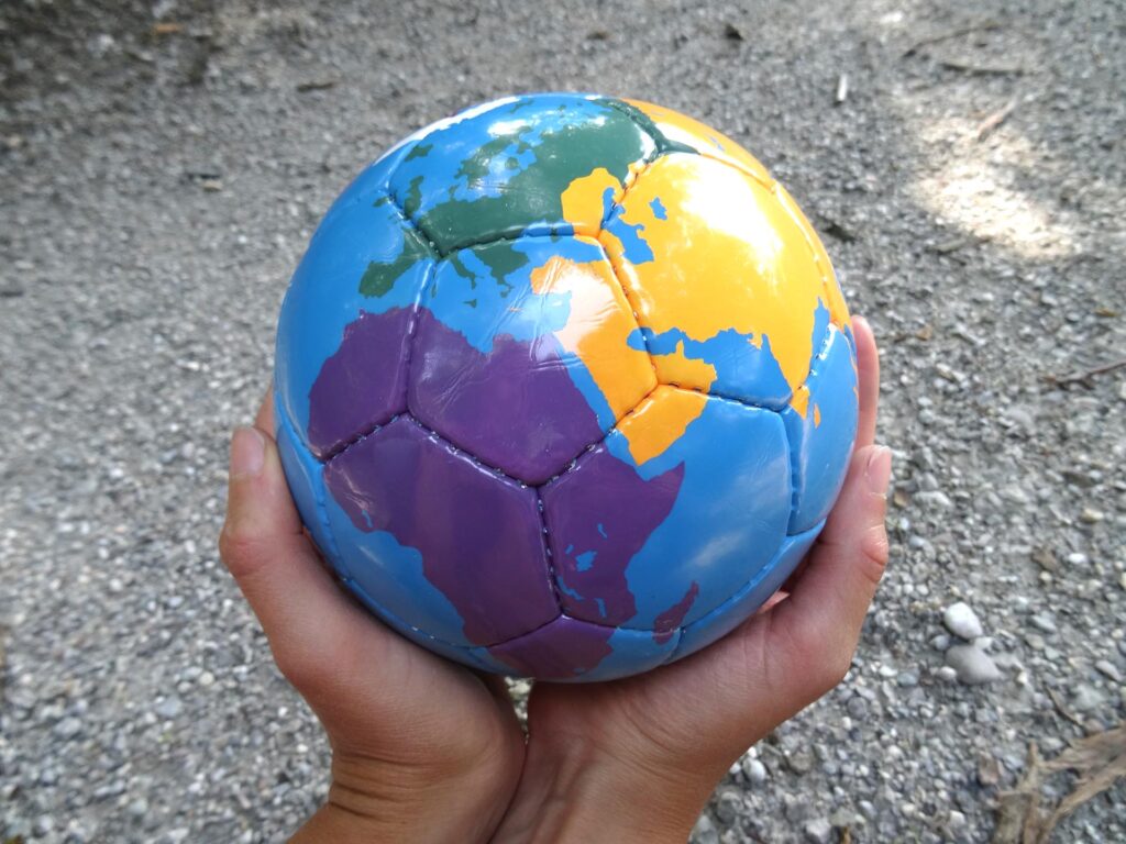 Zwei Hände halten einen Fußball, der als Weltkugel bemalt wurde