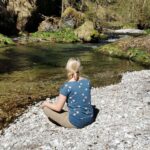 Frau meditiert am Bachbett