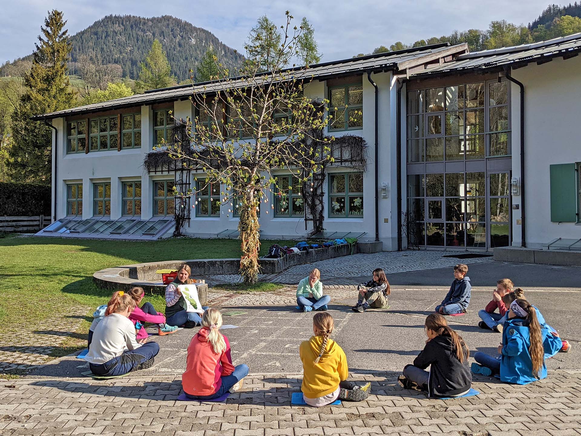 Sitzkreis von Kindern vor der Grundschule Ramsau im Rahmen einer Bildungsveranstaltung