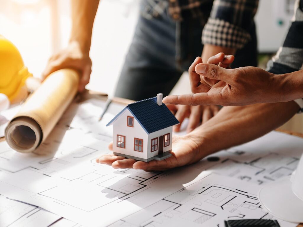 Symbolbild zur Gebäudesanierung mit Bauplan und kleinem Modell eines Wohnhauses