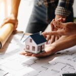 Symbolbild zur Gebäudesanierung mit Bauplan und kleinem Modell eines Wohnhauses