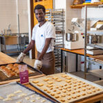 Berufsschüler in der Backstube der Berufsschule mit Blechen voller frisch gebackenem Bergsteigerglück und Hoamat Weckerl